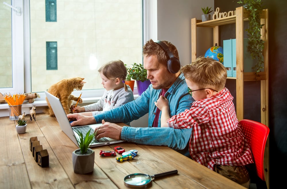Man on laptop working with children playing around