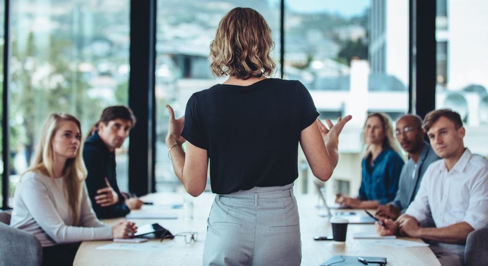 Rear view of a woman explaining new strategies to coworkers during conference meeting in office
