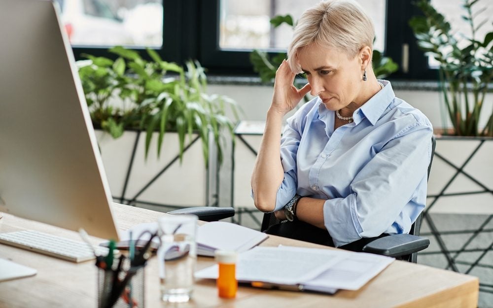 Middle-aged businesswoman with short hair works diligently at her desk in front of a computer during menopause.